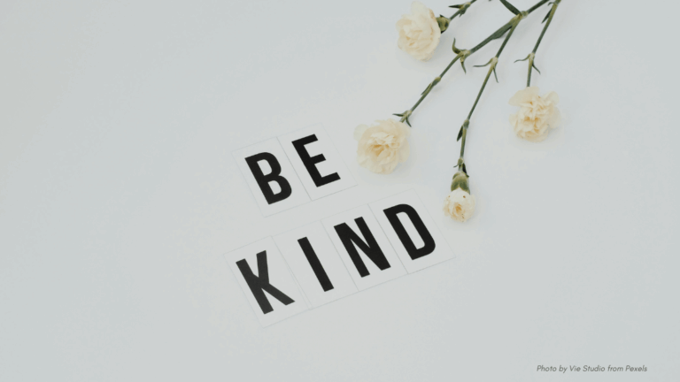 Compassion in Crisis | Black block letters that say "Be Kind" next to pink flowers, mostly white background