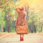 Fall Travel | redhead woman with suit case walking down fall scene on country road