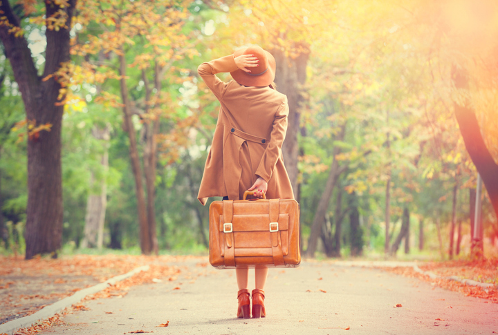 Fall Travel | redhead woman with suit case walking down fall scene on country road