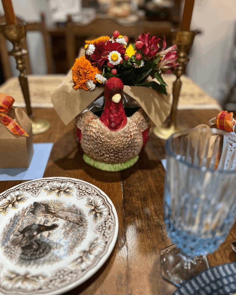 Close up on Thanksgiving table with turkey vase and flowers, china, and gift boxes with orange ribbon for guests