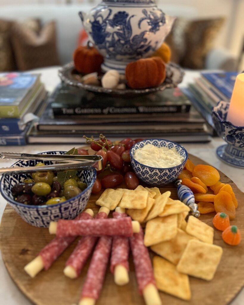 Charcuterie board for Thanksgiving with blue and white dishes, crackers, olives, cheese, apricots, and more