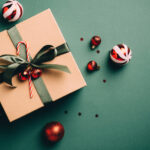 holiday gift giving etiquette | Vintage Christmas present and red balls on dark green background. Retro style Xmas gift box and decorations. Flat lay, top view.