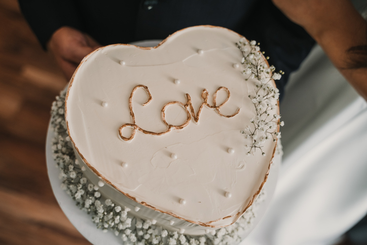 Heart shaped wedding cake with word love written on icing, decorated with white flowers and soft romantic details. Symbol of love, marriage and romantic celebration