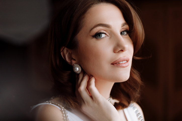 Modern manners and rediscovering the value of thoughtful gestures | beauty concept. portrait of a beautiful young showy brunette woman with bright pin-up make-up and hairstyle. girl in luxury dress and earrings pearls and looking in camera. international women's day.