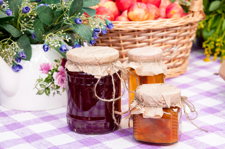 Hostess gift etiquette | jars with jam on tablecloth, basket of fruits and flowers in background
