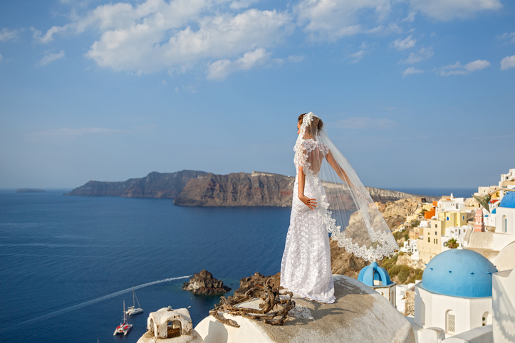 Summer wedding etiquette Q&A | Bride in white dress on the high roof of Santorini, over the sea