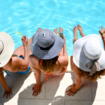 Friendship dilemmas | three women with sun hat sitting by the poolside of a resort swimming pool during summer holiday