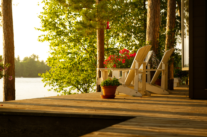 Lake house entertaining etiquette | White Adirondack chairs sits on a cottage wooden deck at sunset looking at the lake. Flower pots are on the deck.