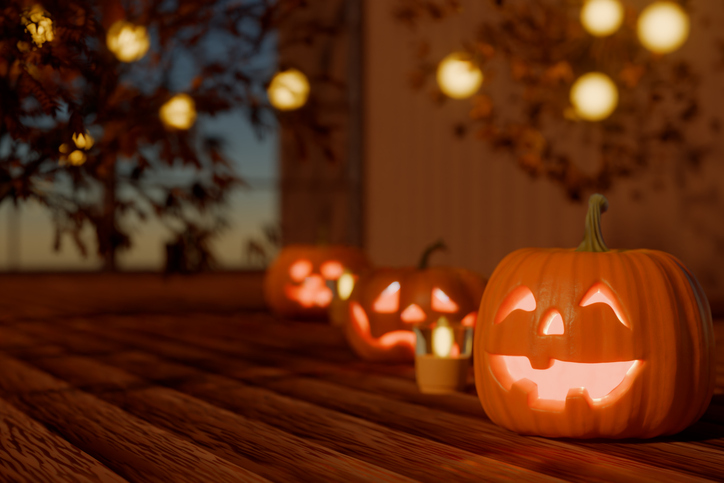 Halloween carved pumpkins glowing on a wooden floor with festive lights in the background. 